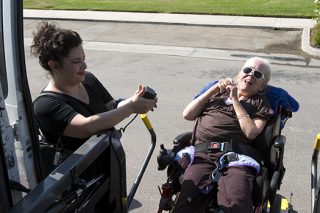 Support staff lower the lift to allow a woman in a wheel chair access to the specialized van.