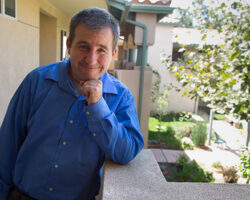 Photo of Chad Brunot standing on the balcony in front of his own home. He has a happy grin.