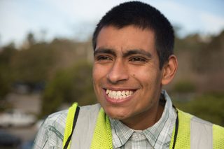 Young man wearing a safety vest with a big white smile while he works in group employment.