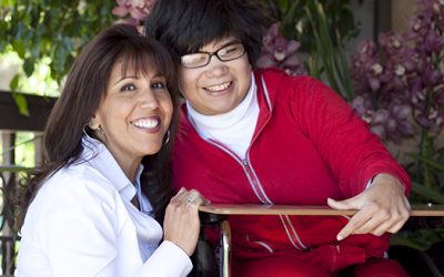 Older sister poses with young woman who has cerebral palsy.