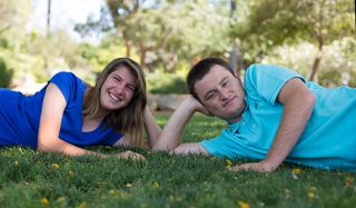 Sister and brother, lay on their sides on the grass and smile.