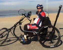 Photo of Jon Seyster on his adapted three-wheel bicycle on the beach.