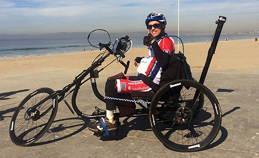 Photo of Jon Seyster on his adapted three-wheel bicycle on the beach.