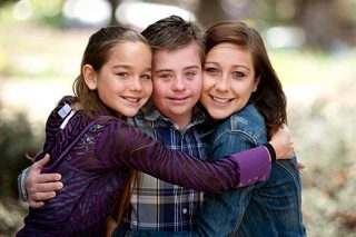 Three siblings, all in hugging together and smiling.