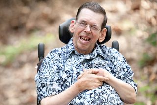 A man with cerebral palsy smiling while sitting in a wheel chair.