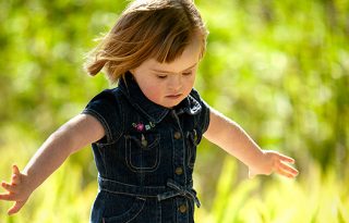 Toddler girl spins with her arms out in the sunshine.