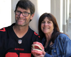 TCRC's dental coordinator Kayla holds up a model of teeth while posing with a person served at a dental clinic