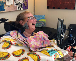 Photo of Jamie Burba, author and cancer survivor laughing as she wears assistive tech.