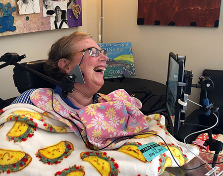 Photo of Jamie Burba, author and cancer survivor laughing as she wears assistive tech.