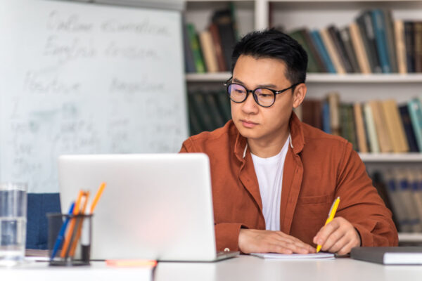 A Service Provider in his office looks at his laptop and takes notes during a zoom meeting