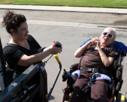 A senior white woman with cerebral palsy waits for the lift of an adapted van