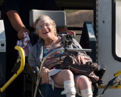 Senior woman smiles with joy and clutches her bag as she exits the adapted bus