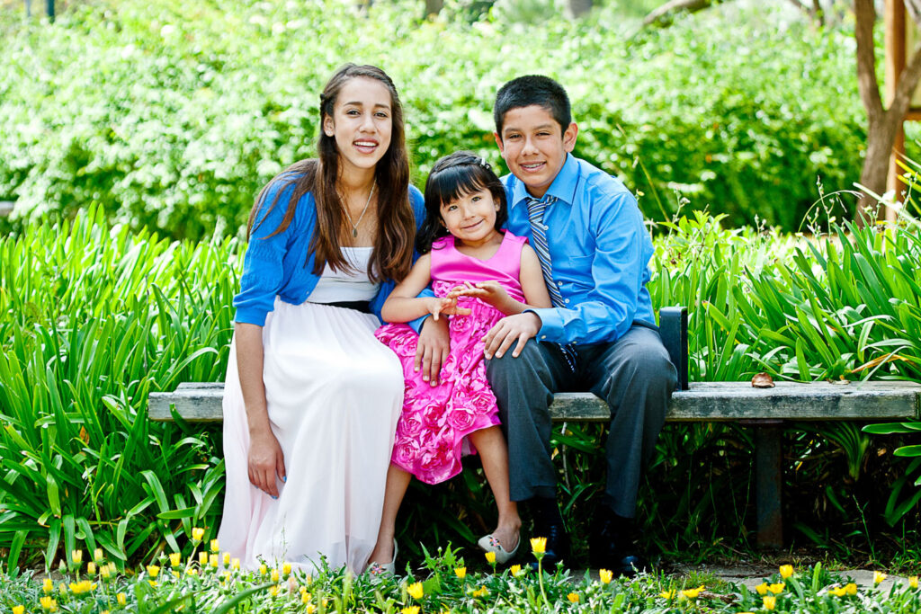 Three young siblings smile from a bench in the park