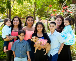 Hispanic mom poses with her eight kids and grandkids. A young girl holds a chihuahua wearing a flowered shirt