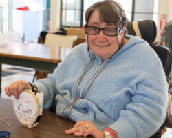 Ingelise works on a small round needlepoint at Alpha's Slingshot Gallery