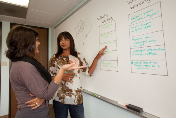 A service provider and her colleague do a "working, not working" exercise on a large whiteboard