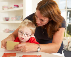 A woman does speech therapy with a young boy who has Down Syndrome