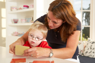 A woman does speech therapy with a young boy who has Down Syndrome