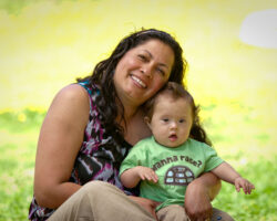 woman holding her infant who has Down Syndrome and smiling in a field of yellow