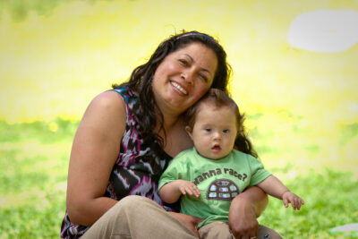 woman holding her infant who has Down Syndrome and smiling in a field of yellow