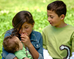 Two young siblings hold their infant brother who has Down Syndrome, the girl kisses his hand