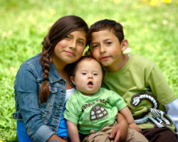 Two young siblings hold their infant brother who has Down Syndrome