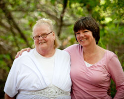 A care-giver puts her arm around a person served in the park