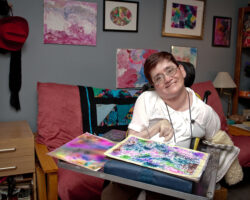 Woman painter who uses a wheelchair poses with her artwork