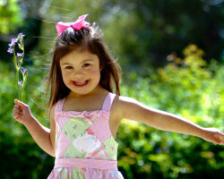 Three year old girl with down syndrome smiles while holding flower