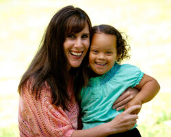 Mom holds toddler daughter with big smiles on a light yellow background