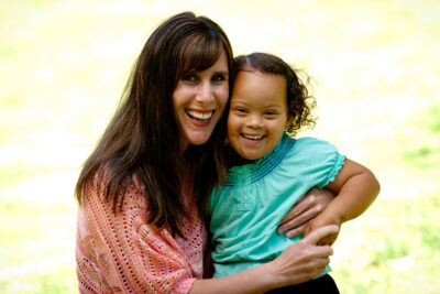 Mom holds toddler daughter with big smiles on a light yellow background