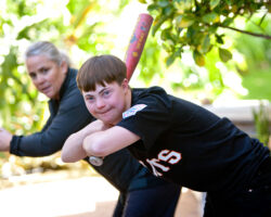 Young man with Down Syndrome practices holding a baseball bat with his care-giver