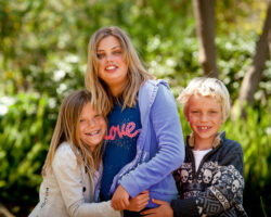 Teenage sister hugs younger sister as brother stands in