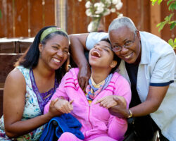 Grandmother and mom hug daughter in wheelchair