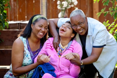 Grandmother and mom hug daughter in wheelchair