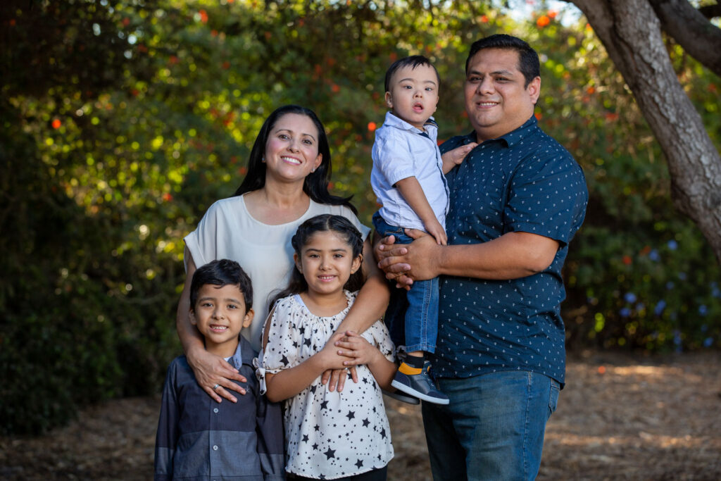 Hispanic family of five portrait in the park. Dad holds youngest with Down Syndrome