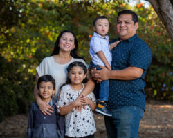 Hispanic family of five portrait in the park. Dad holds youngest with Down Syndrome