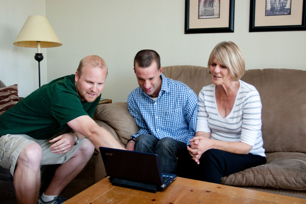 Mom and her adult son look at laptop with his care giver