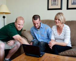 Mom and her adult son look at laptop with his care giver