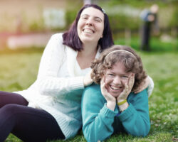 portrait of happy women with disabilities on lawn, leaning against one another