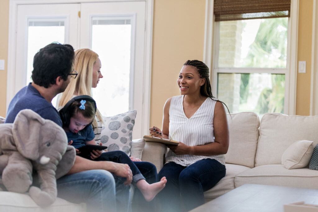 Service Coordinator sits with young couple and their child in their home