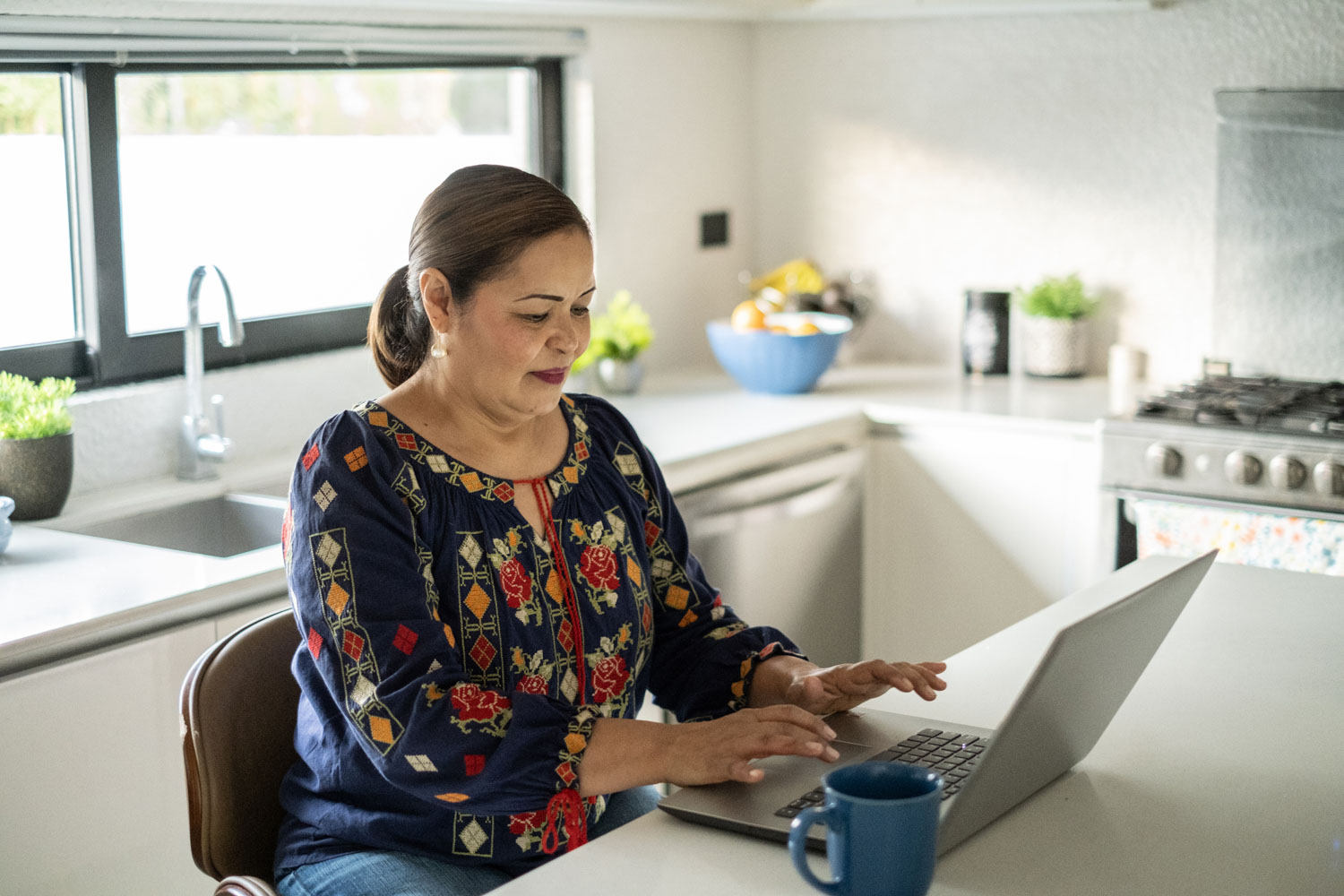 Hispanic mom sits in kitchen and takes a survey on her laptop