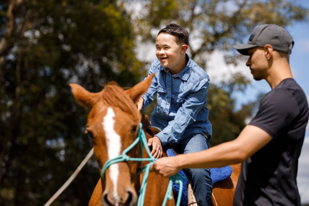 Boy with down syndrome riding a horse at camp with support staff