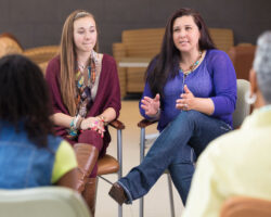 Two women sitting in support group circle, sharing.