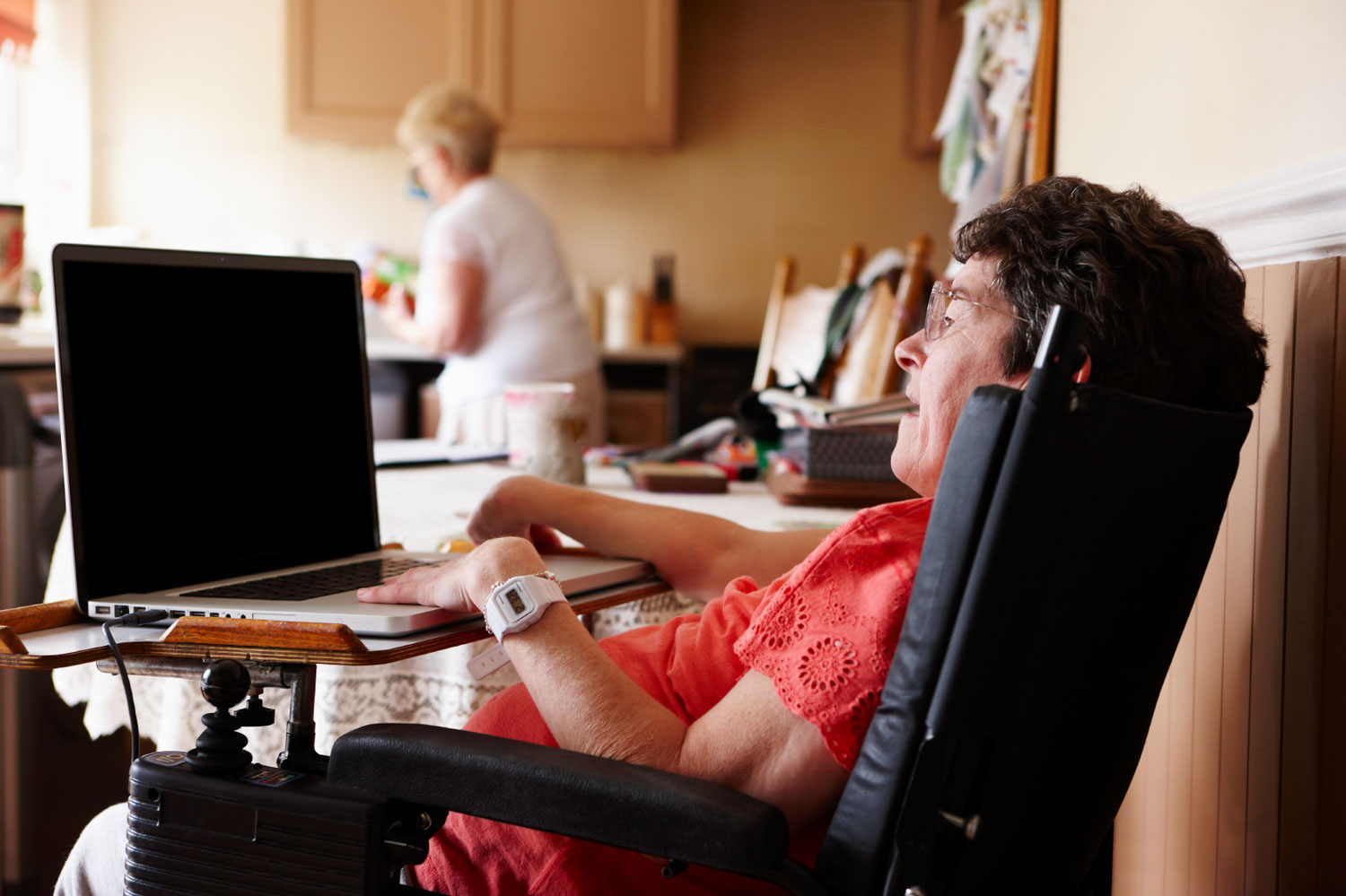 Woman with cerebal palsy works on her laptop as a helper does the dishes