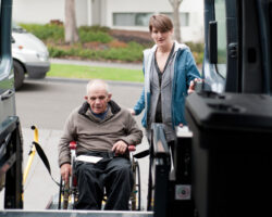 Older man in a wheelchair being helped into a van