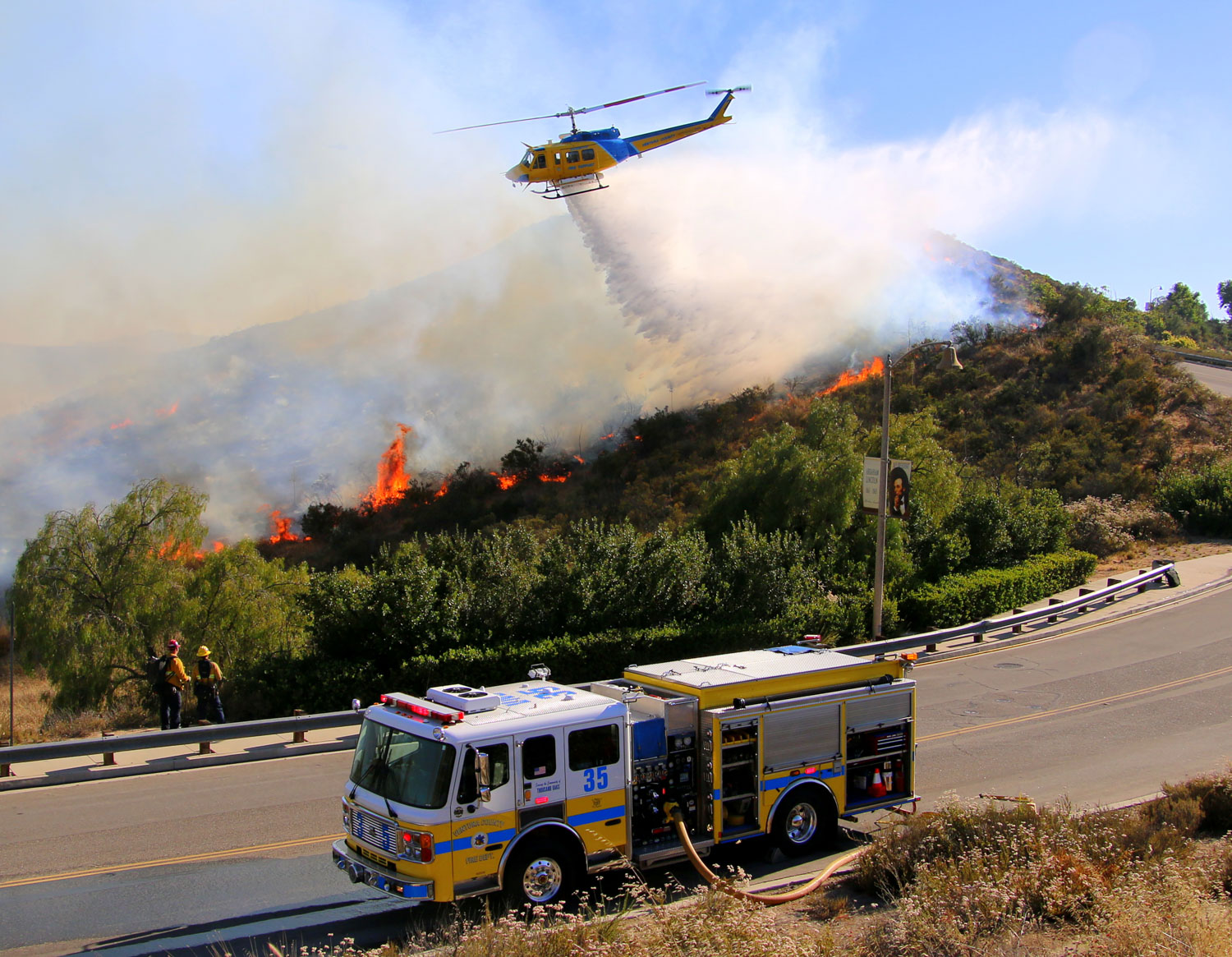 Fire engine in the back country as helicopter drops water on active fire, daytime